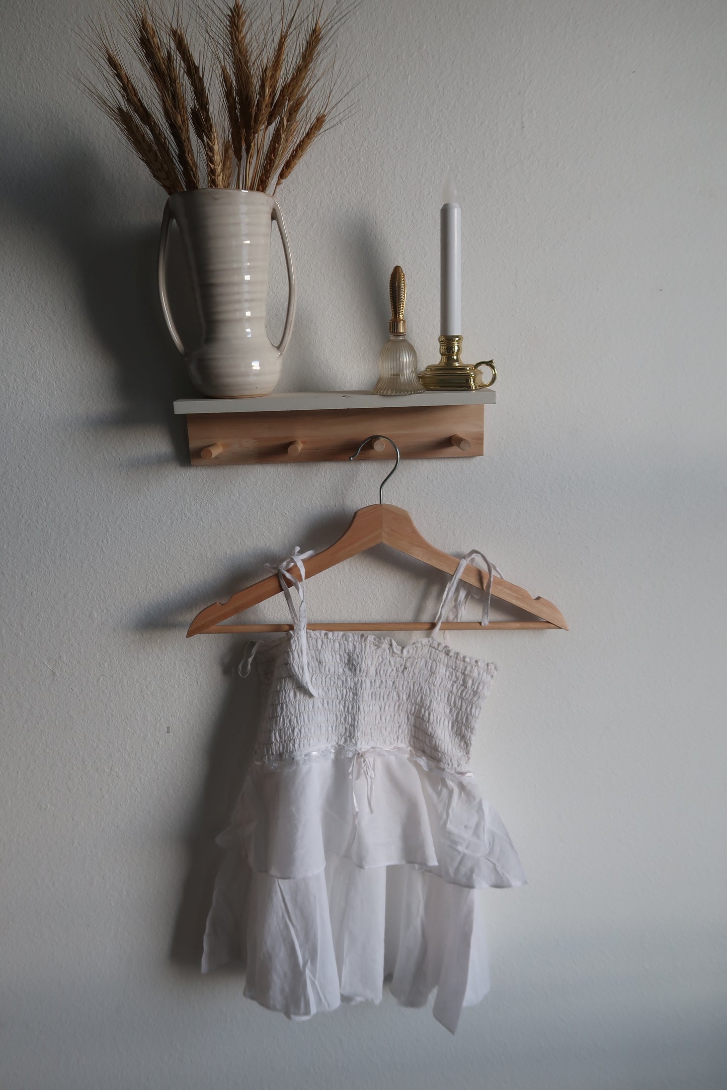 White dress on a wooden hanger with a vase and decorative items on a light gray background