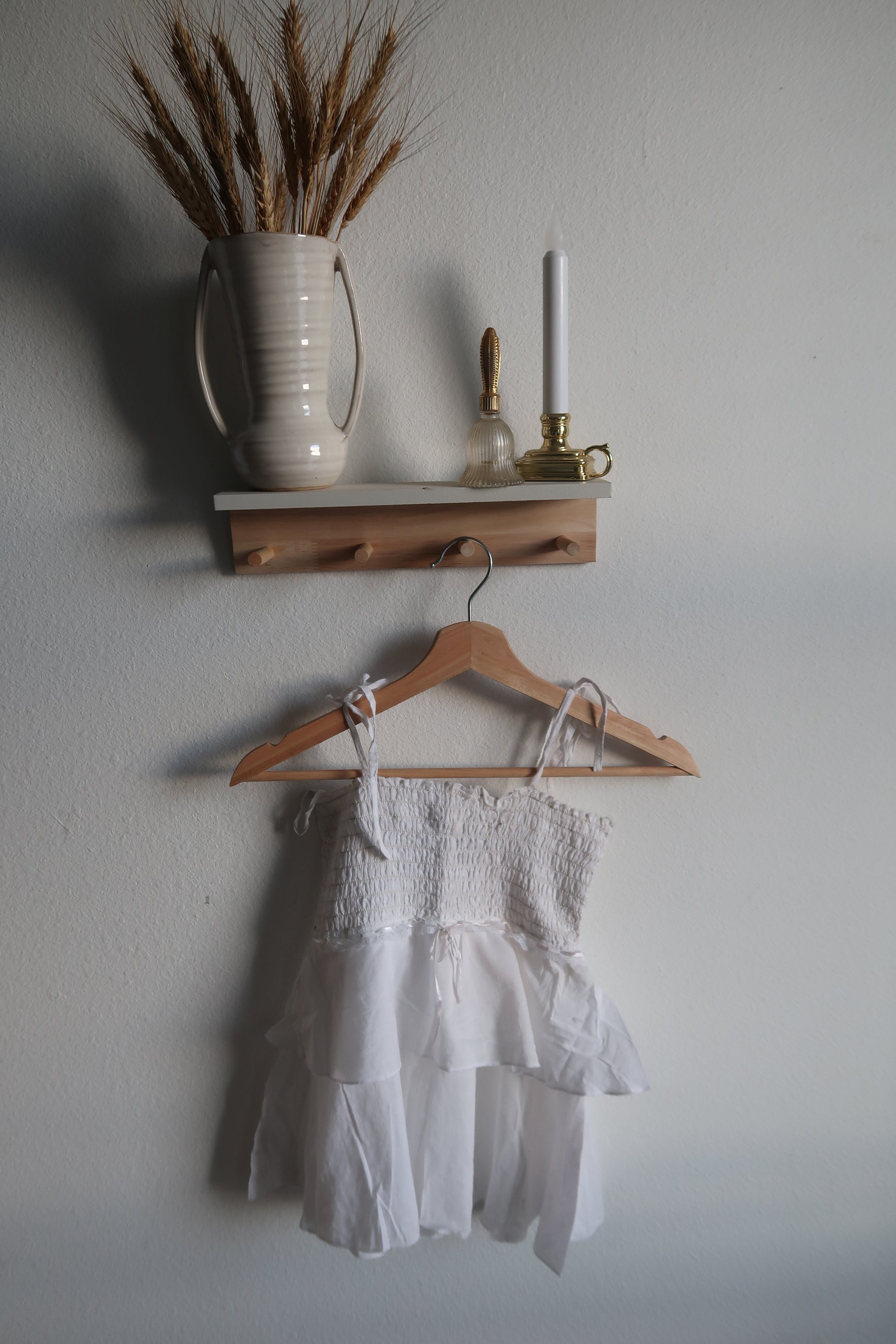 White dress on a wooden hanger with a vase and decorative items on a light gray background